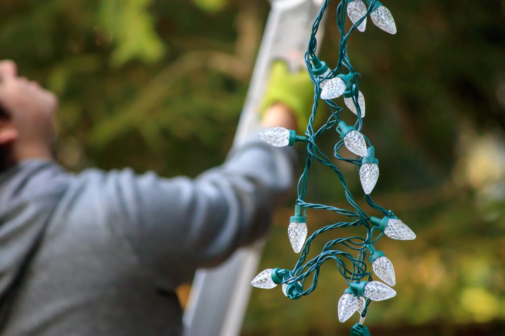 man hanging holiday lights on house